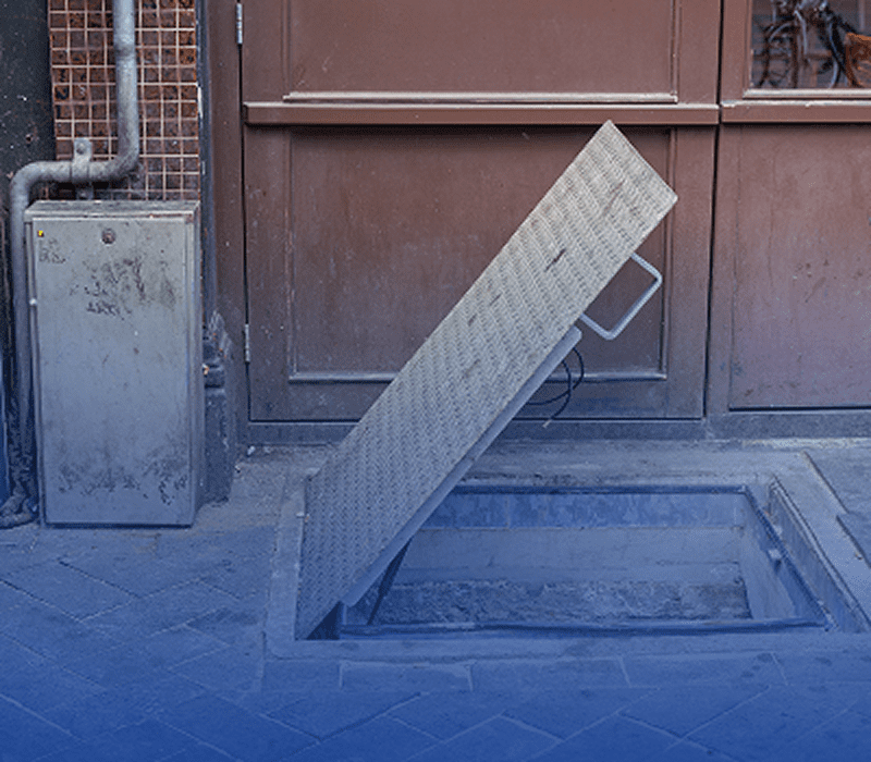 Open metal hatch on urban sidewalk.